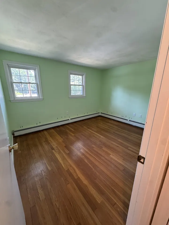 Manchester, NH bedroom with green walls and a worn, orange-toned hardwood floor before LCH refinished it